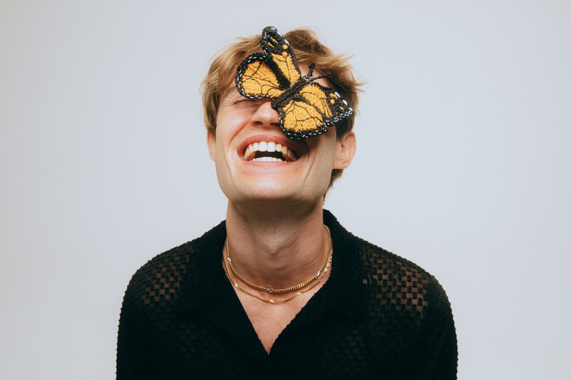 Ein Bild von Henri Purnell, dem Produzenten, Sänger und Influencer. mit einem gehäkelten Schmetterling im Gesicht.